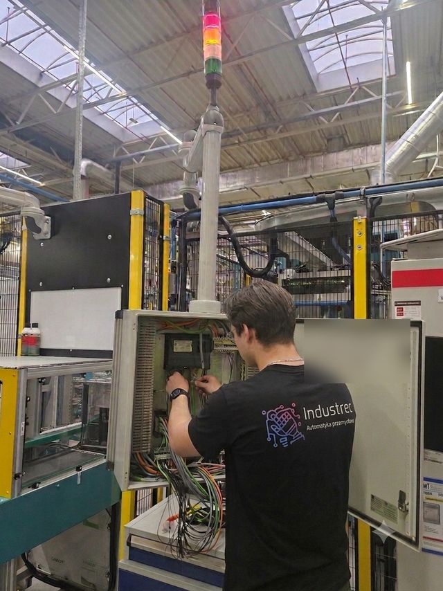 Technik Industrec podłącza przewody w otwartej szafie sterowniczej maszyny na linii produkcyjnej